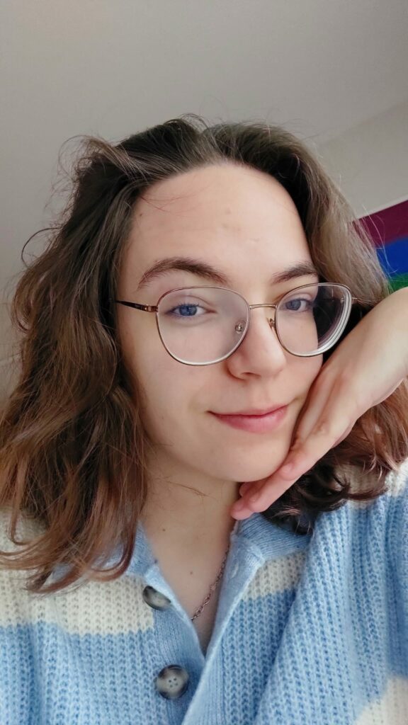 woman with medium wavy hair and glasses, wearing a baby blue and white striped knitted sweater