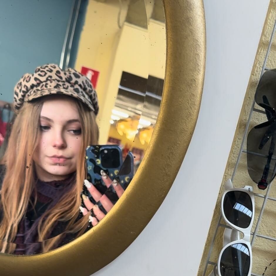 A woman taking a selfie in a mirror with a leopard-print hat. 