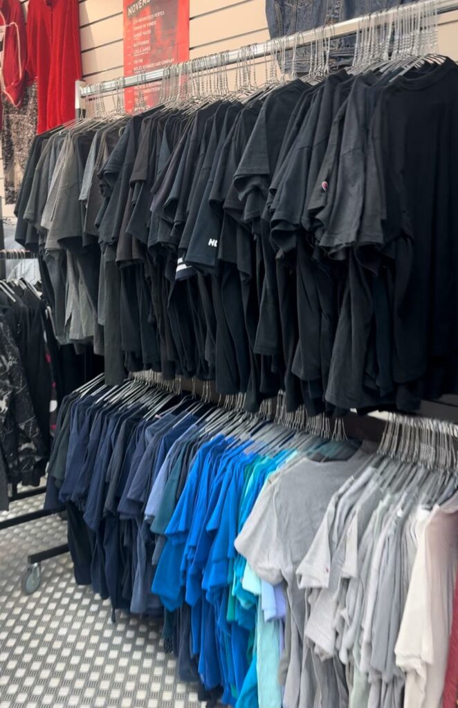 A clothing rack with a lot of shirts, most of them are black, but there are also blue, grey and white ones. 