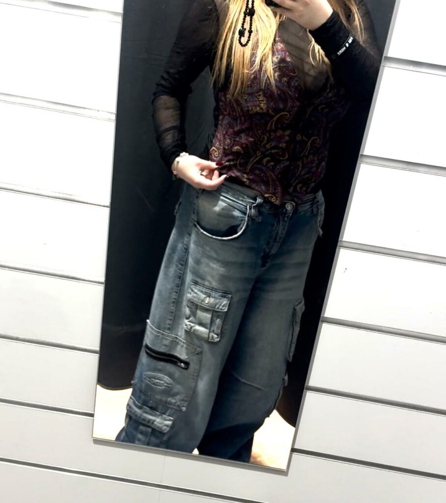 A woman taking a selfie in the mirror wearing a vest with a colourful pattern. 