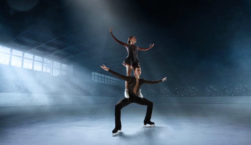 An figure skating pair. The woman standing on the mans legs, while being on ice. 